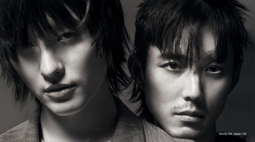 Woods and Justin H. Min pose in moody lighting, teasing their mystery short film “Slide Strum Mute” ahead of its February 26 release.